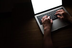 木の机の上でノートパソコンのキーボードを打つ手元